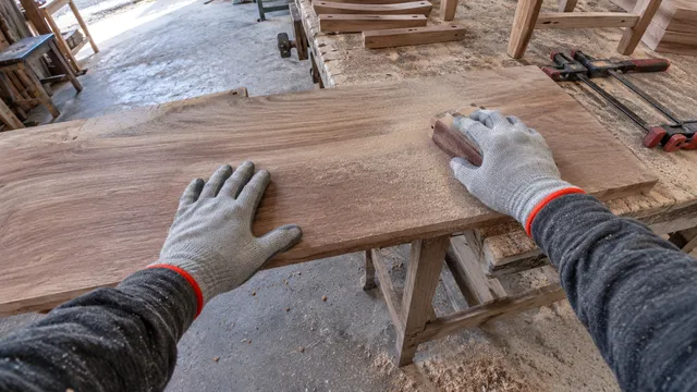 Cámara 8: una mano sujeta una tabla mientras la otra la lija con un taco de lija.